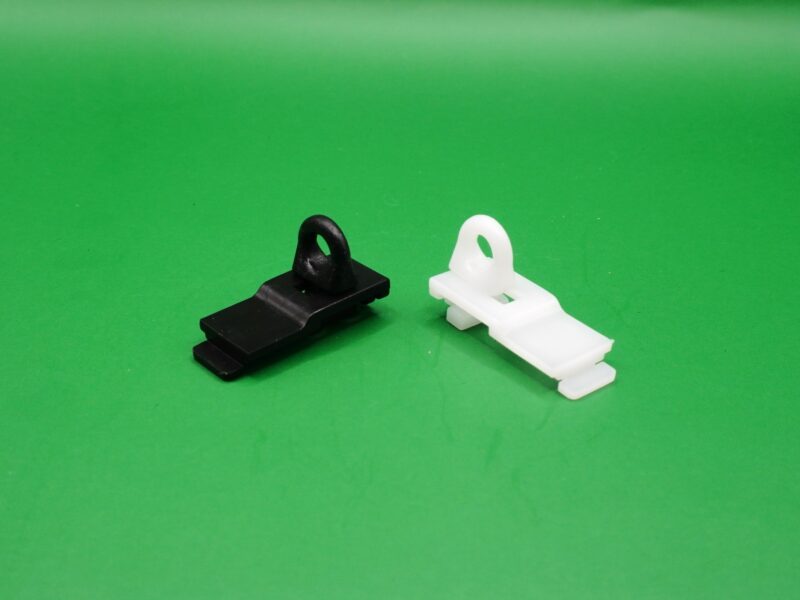 Zwei Endfeststeller aus Kunststoff in Schwarz und Weiß auf grünem Hintergrund, geeignet für Gardinenschienen mit 6 mm Lauf.